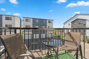 Een balkon met buitenmeubilair, een glazen tafel en uitzicht op moderne gebouwen.