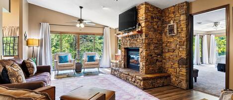Un salón amplio con chimenea de piedra, sofás de cuero y un ventanal con vistas al exterior.
