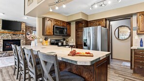 A modern kitchen with a large island, wooden cabinets, a built-in microwave, and a stainless steel refrigerator. - Creek & Green by Avantstay Creekside Hot Tub + Pool Table Golf Course Views (Gatlinburg)
