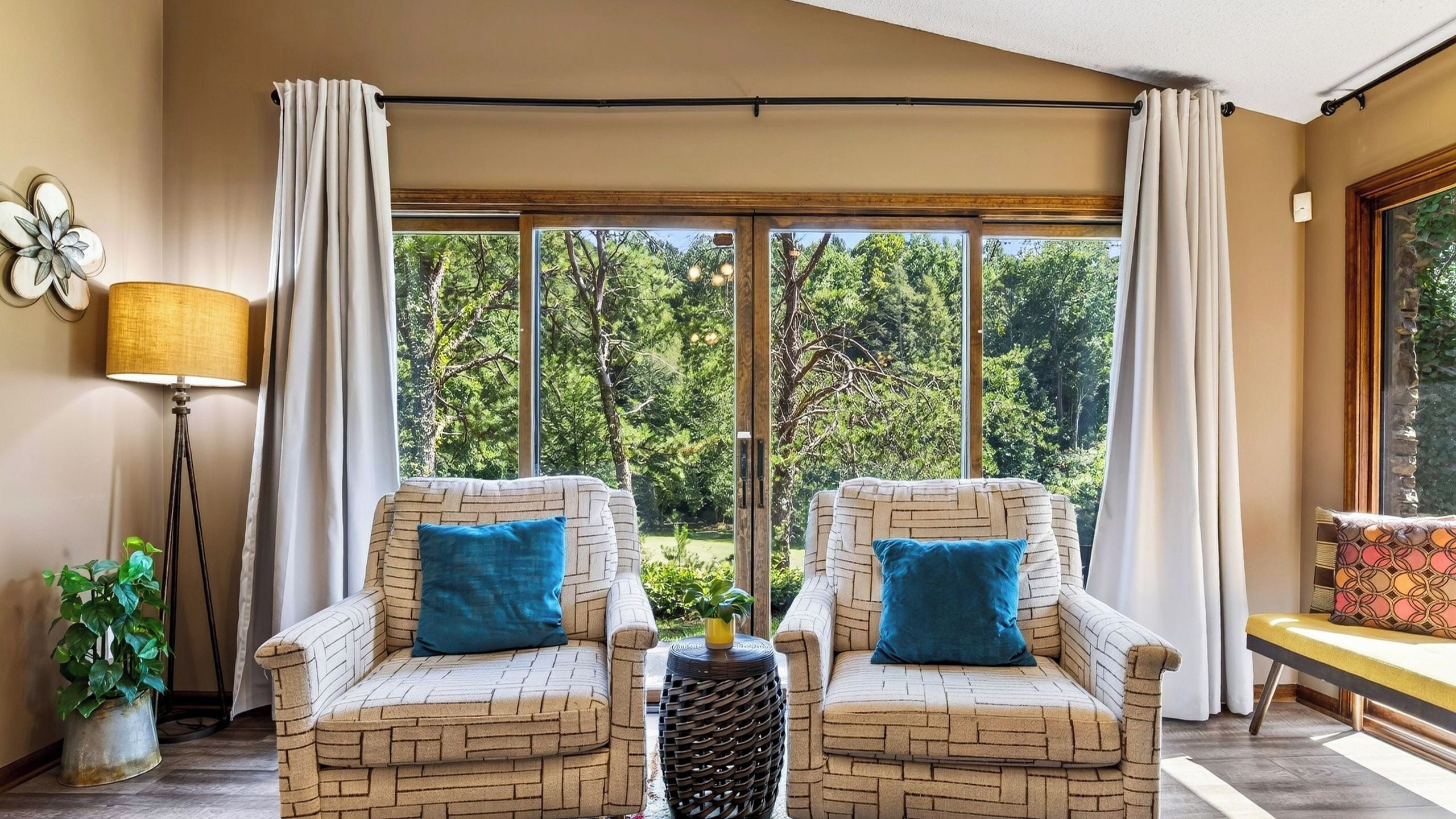 A room with two brick-patterned armchairs, a floor lamp, and a view of a green landscape through large windows.