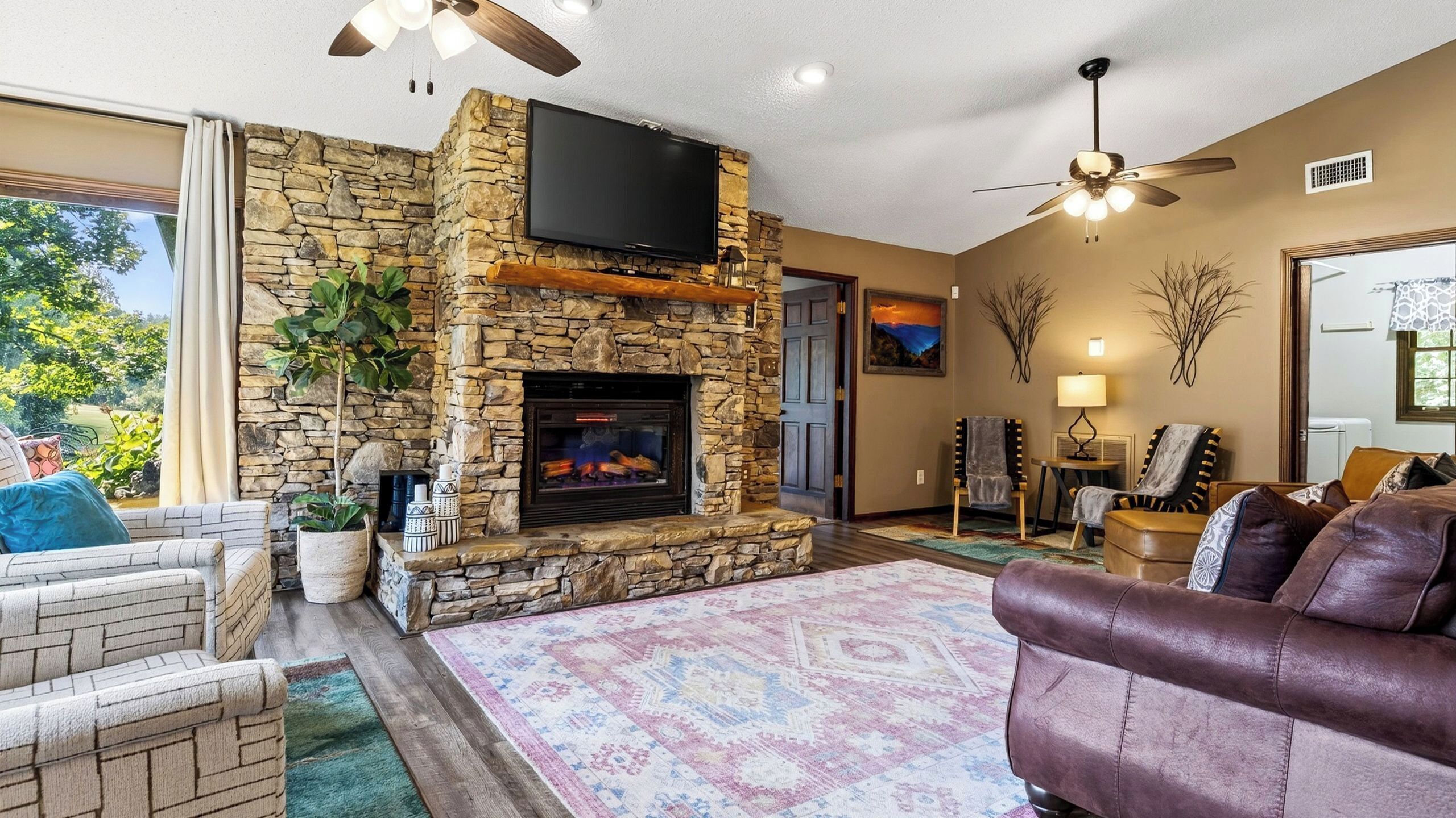 A living room with a stone fireplace, a flat-screen TV, and a large window.