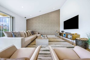 A modern living room with a sofa set, a coffee table, a TV mounted on the wall, and a patterned rug. - Calumet Luxury Paradise  – A Sophisticated La Jolla Retreat (San Diego)