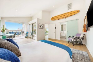 A modern bedroom with a large bed, a view to the outside, and a surfboard mounted on the wall. - Calumet Luxury Paradise  – A Sophisticated La Jolla Retreat (San Diego)