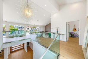 A modern interior with a glass staircase, a hanging light fixture, and a view of the outside. - Calumet Luxury Paradise  – A Sophisticated La Jolla Retreat (San Diego)