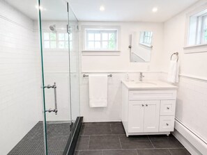 Ein modernes Badezimmer mit Duschkabine aus Glas, einem weißen Waschtisch mit Spiegel und einem Fenster für natürliches Licht.
