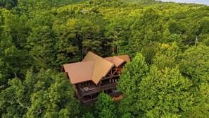 A cabin with a sloped roof, surrounded by dense forest. - Dreaming Bear Cabin by Avantstay Hot Tub Deck Game Room Soaking Tubs Near Nat'l Park Entry (Gatlinburg)