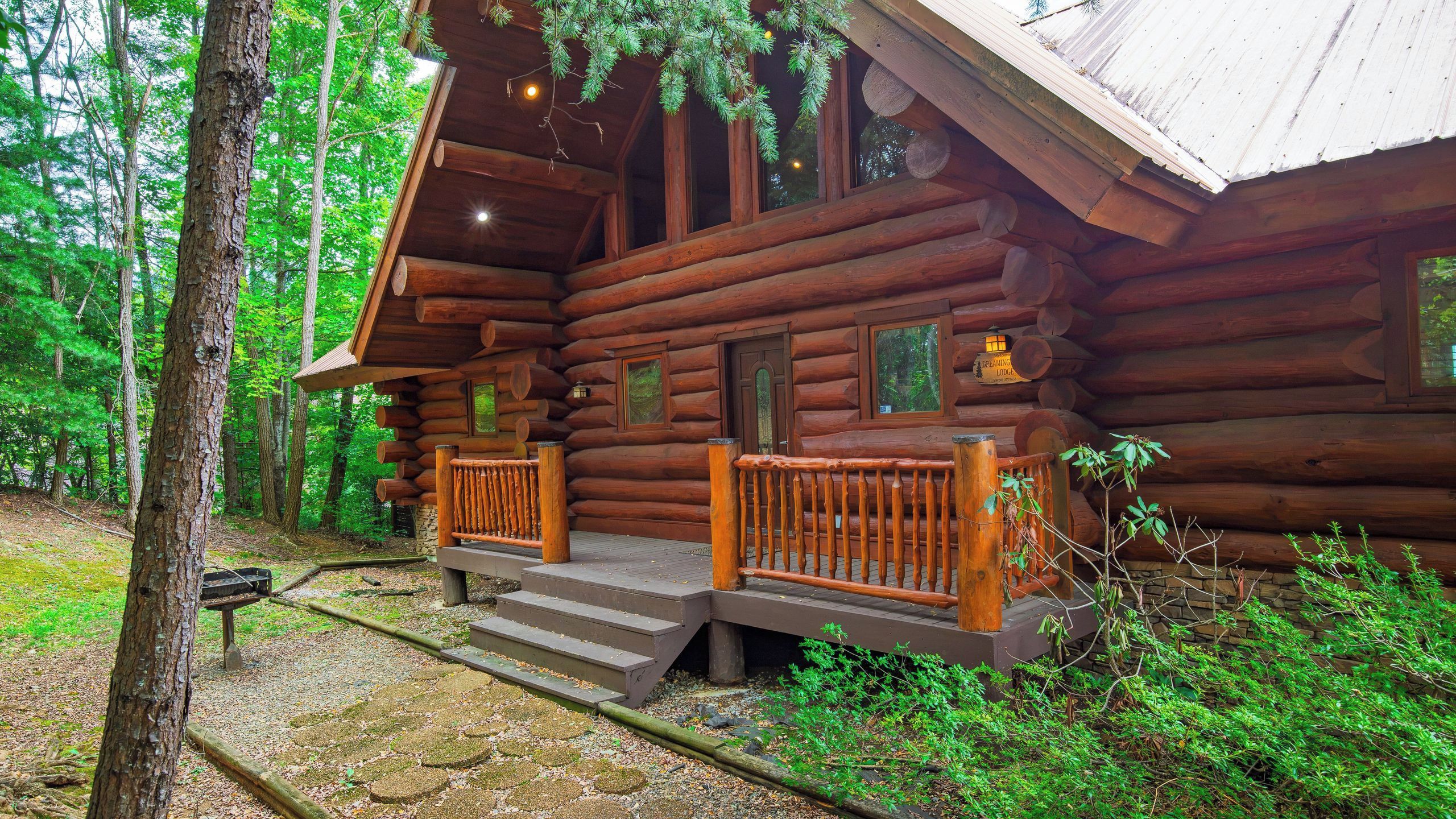 A log cabin with a porch, steps leading to the entrance, and a sign indicating it's a 'Dreaming Lodge'.