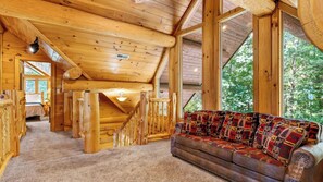 Ein Blockhaus-Interieur mit einer Holztreppe, einer Couch mit gemusterten Kissen und Blick ins Grüne.