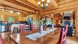 A spacious kitchen with wooden cabinets, a stainless steel refrigerator, and a dining area with a wooden table and chairs. - Dreaming Bear Cabin by Avantstay Hot Tub Deck Game Room Soaking Tubs Near Nat'l Park Entry (Gatlinburg)