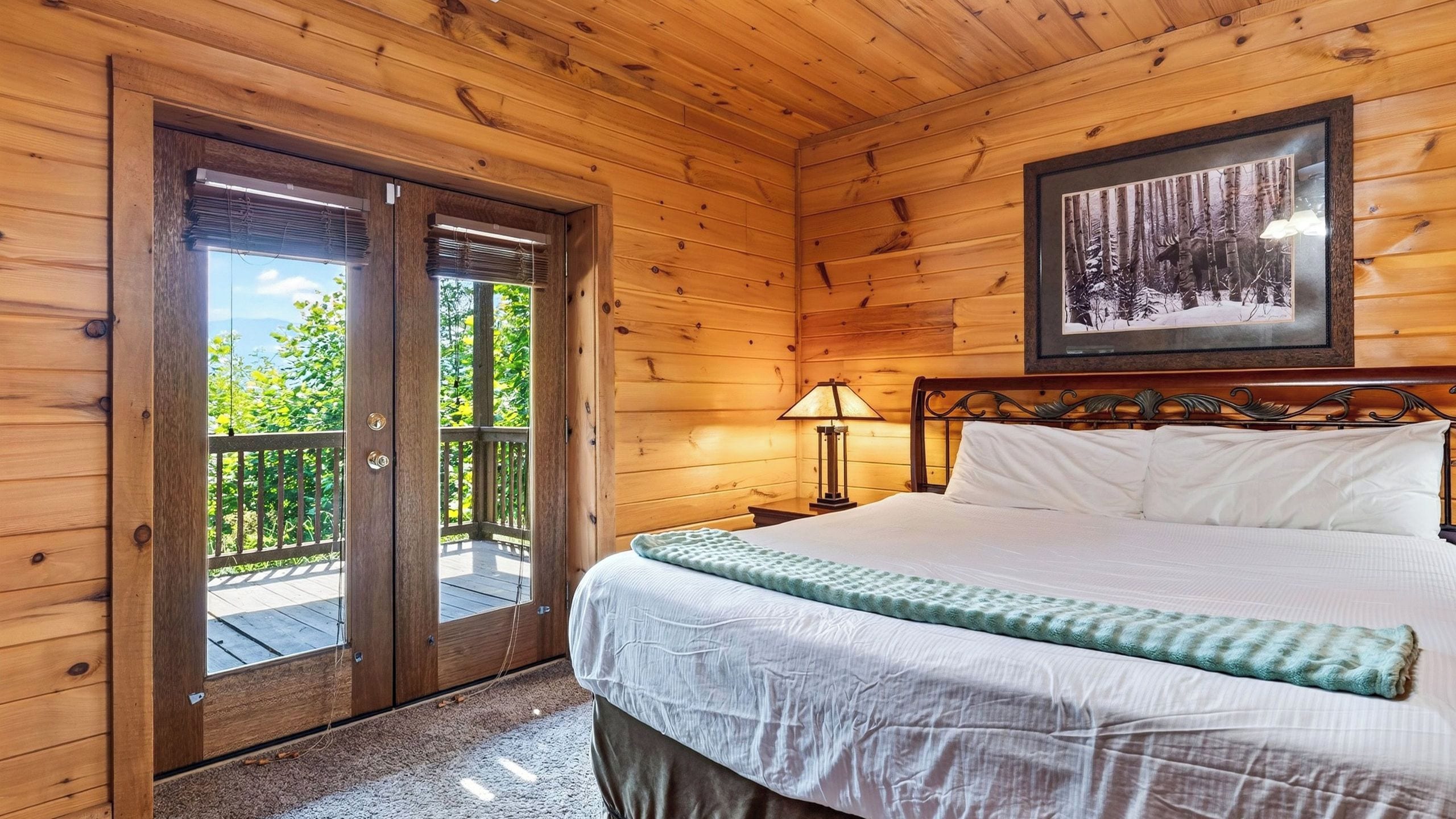 Quarto de cabana de madeira com cama, mesa de cabeceira, abajur e quadro na parede.