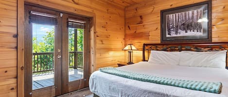 Ein Zimmer einer Holzhütte mit einem Bett, einem Nachttisch, einer Lampe und einem gerahmten Bild an der Wand.