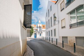 En smal gade med bygninger langs begge sider, en blå dør og en kirke med et spiret i det fjerne.