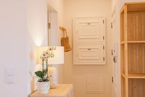 En gang med en trædør, en lyskontakt på væggen og et lille bord med en lampe og en potteplante.