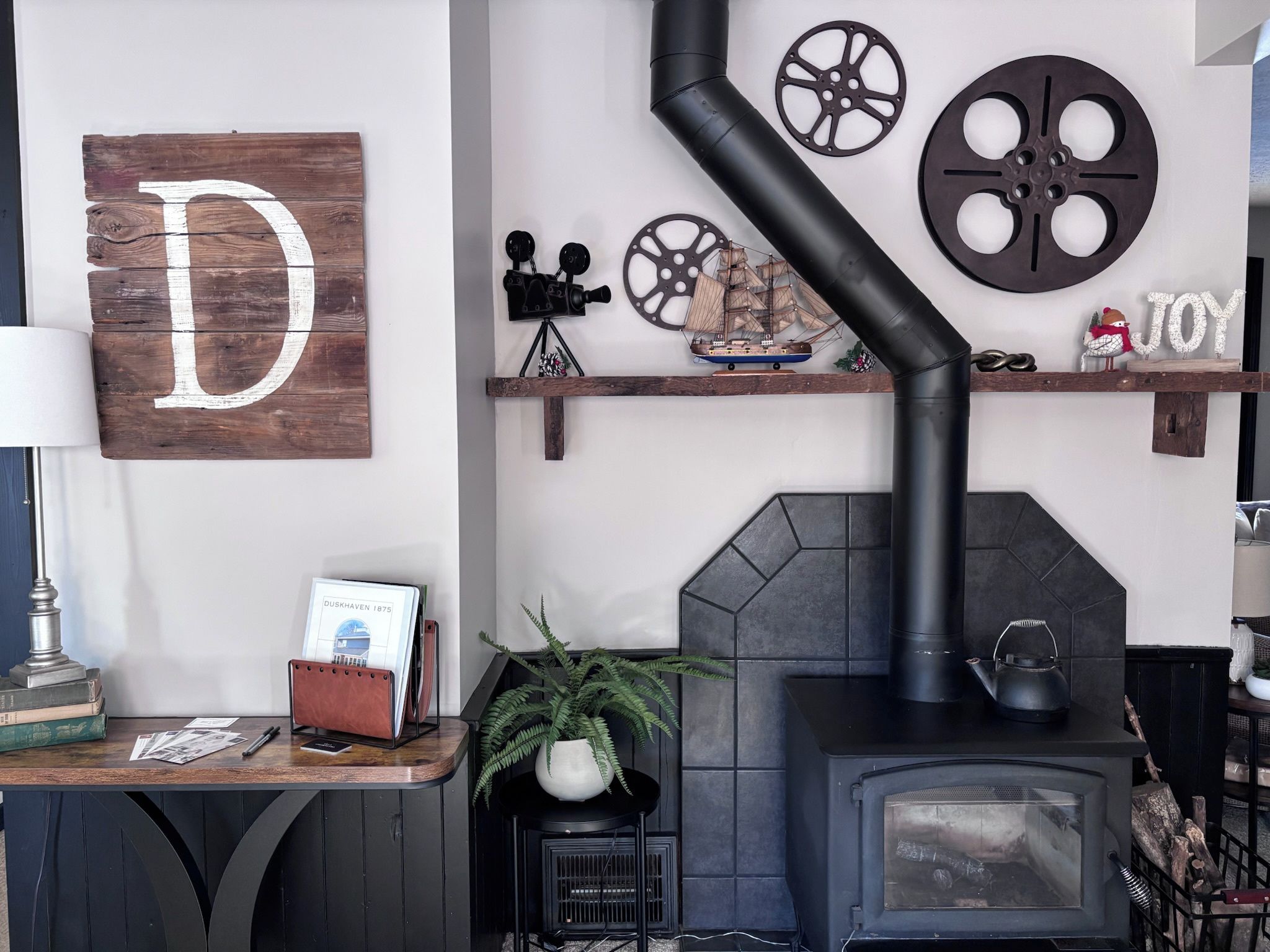 Een gezellige kamer met een open haard, een houten bord met een grote letter D, en decoratieve spullen op planken.