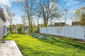 A backyard with a white fence, a grassy lawn, and several green planters.