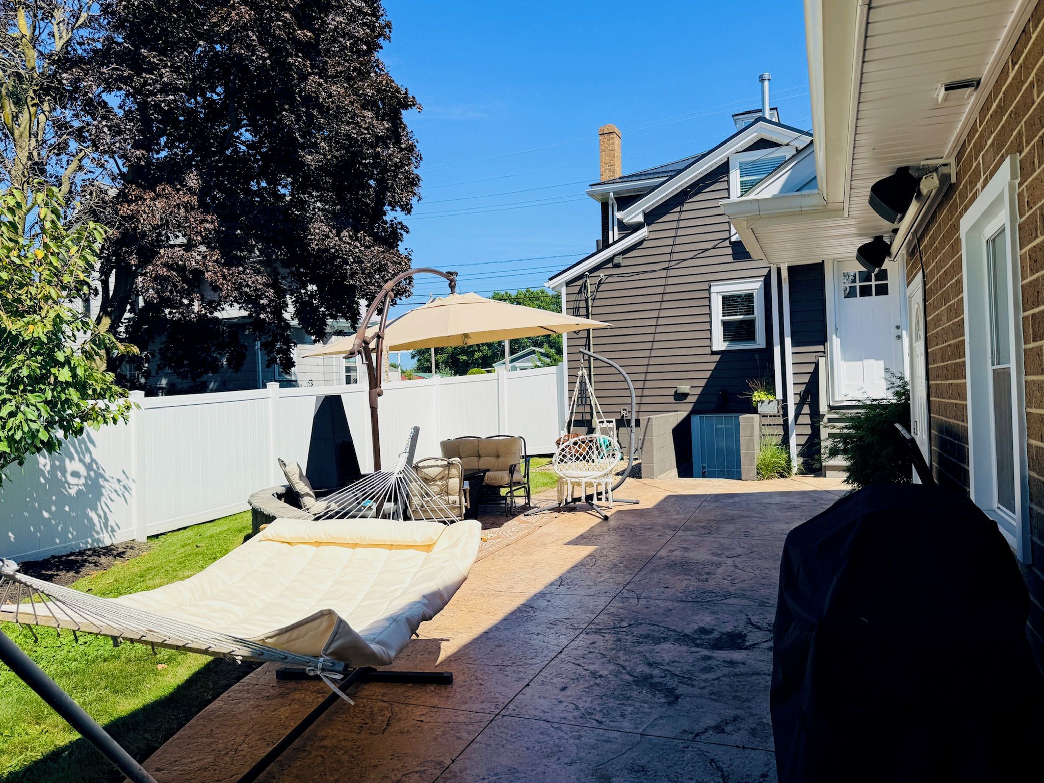 Un jardin avec un hamac, des meubles de patio et un espace salon abrité.