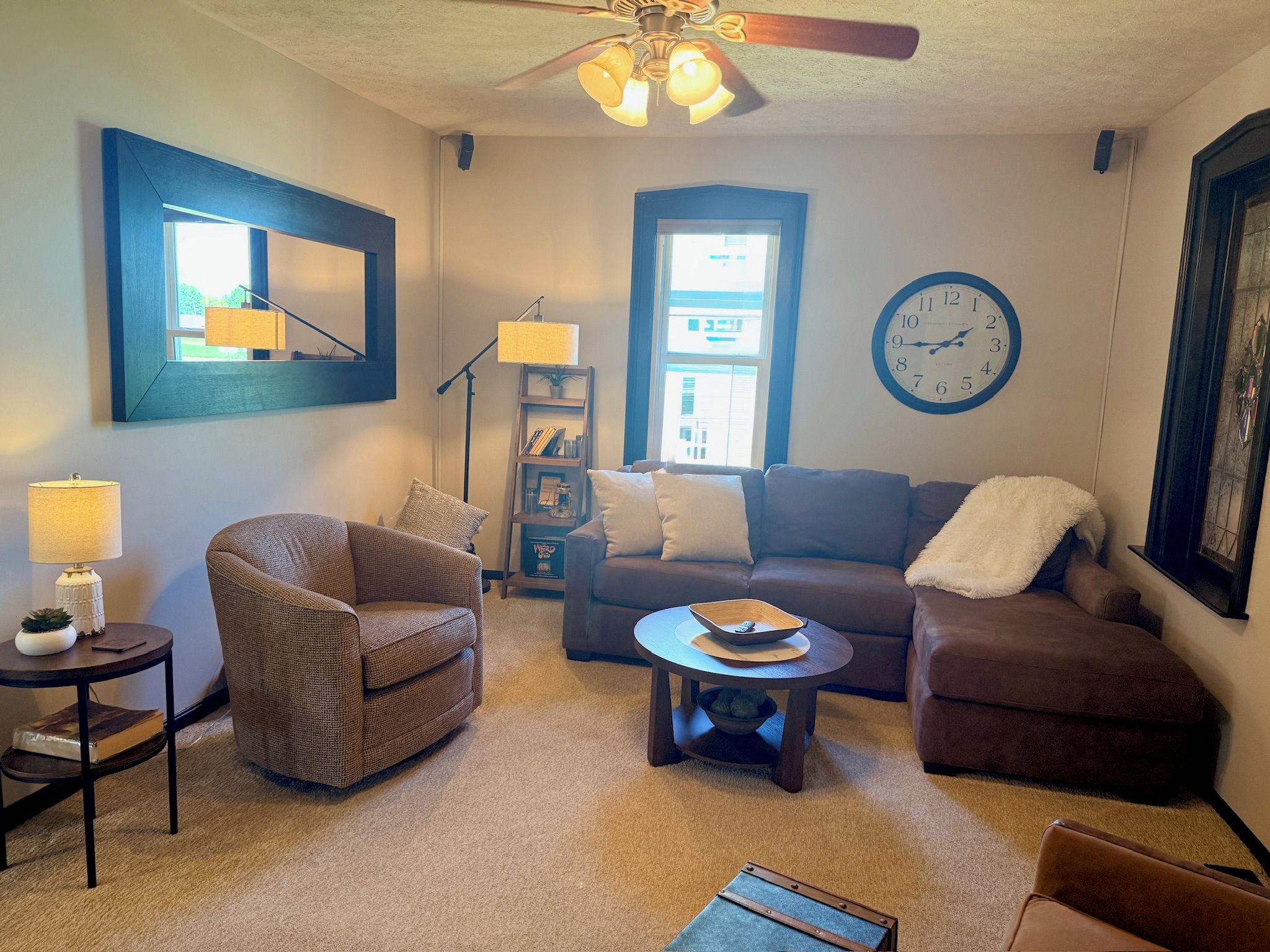 A living room with a sofa, armchair, coffee table, and a clock on the wall.