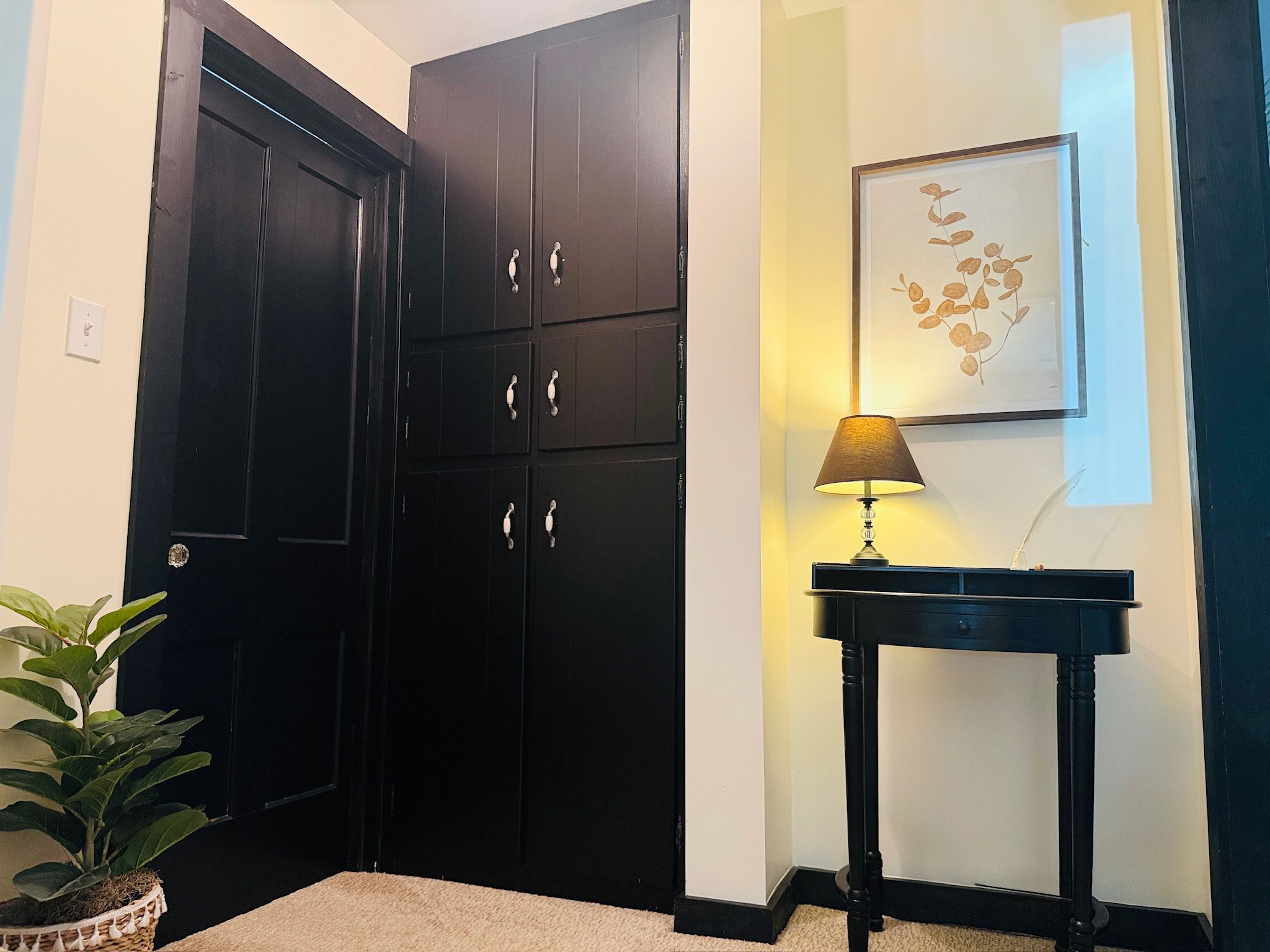 A corner with a black door, a small table with a lamp, and a framed picture on the wall.
