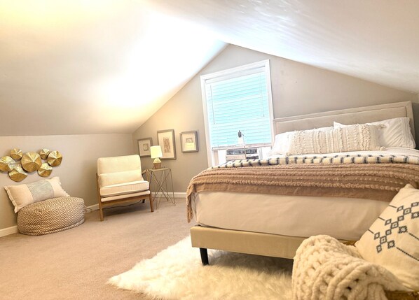 A bedroom with a bed, a chair, a small table, and a window.