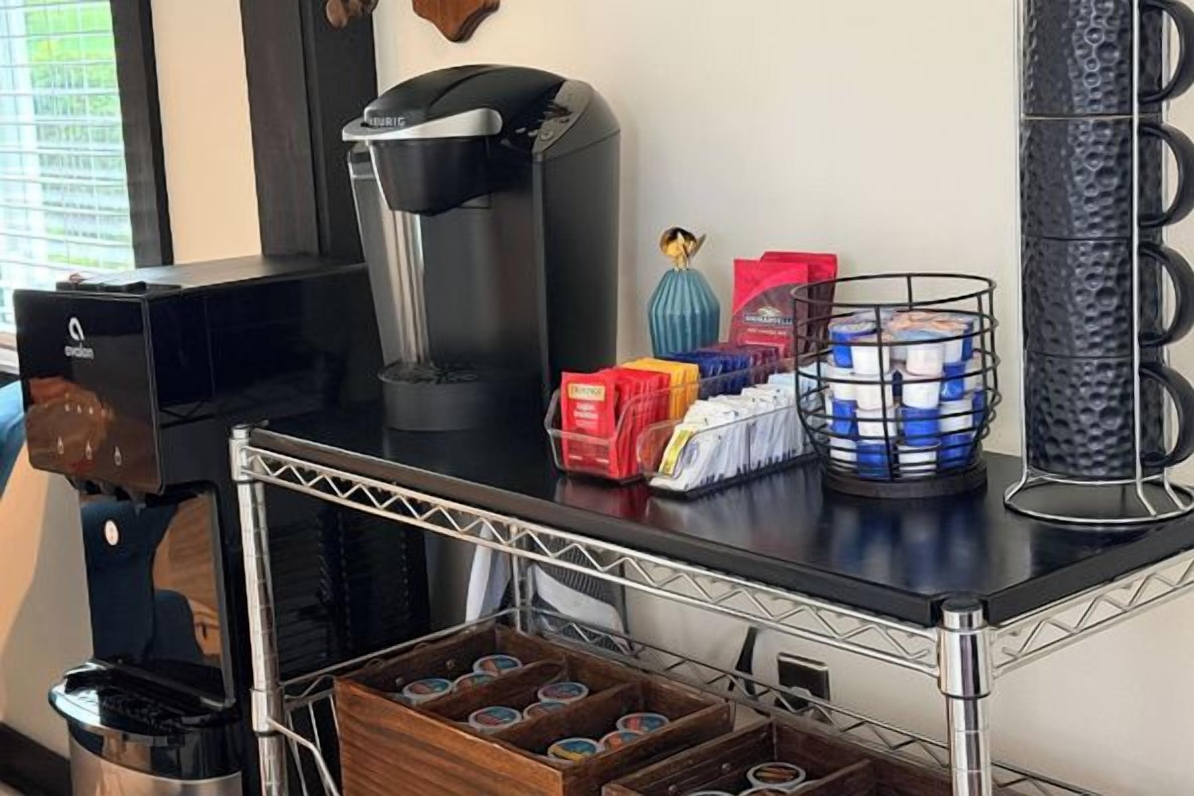 A coffee station with a coffee machine, a basket of coffee pods, and a coffee grinder.