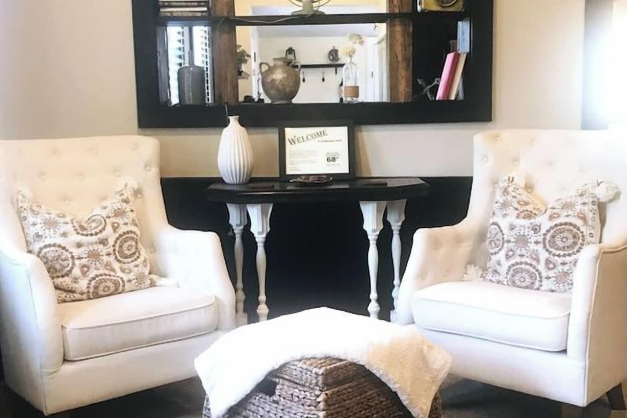 A room with two white armchairs, a small table, and a mirror above.