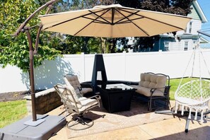 An outdoor patio with a grill, two cushioned chairs, a hanging chair, and a large umbrella. - Private Estate | Historic Home + Industrial Studio (Uniontown)