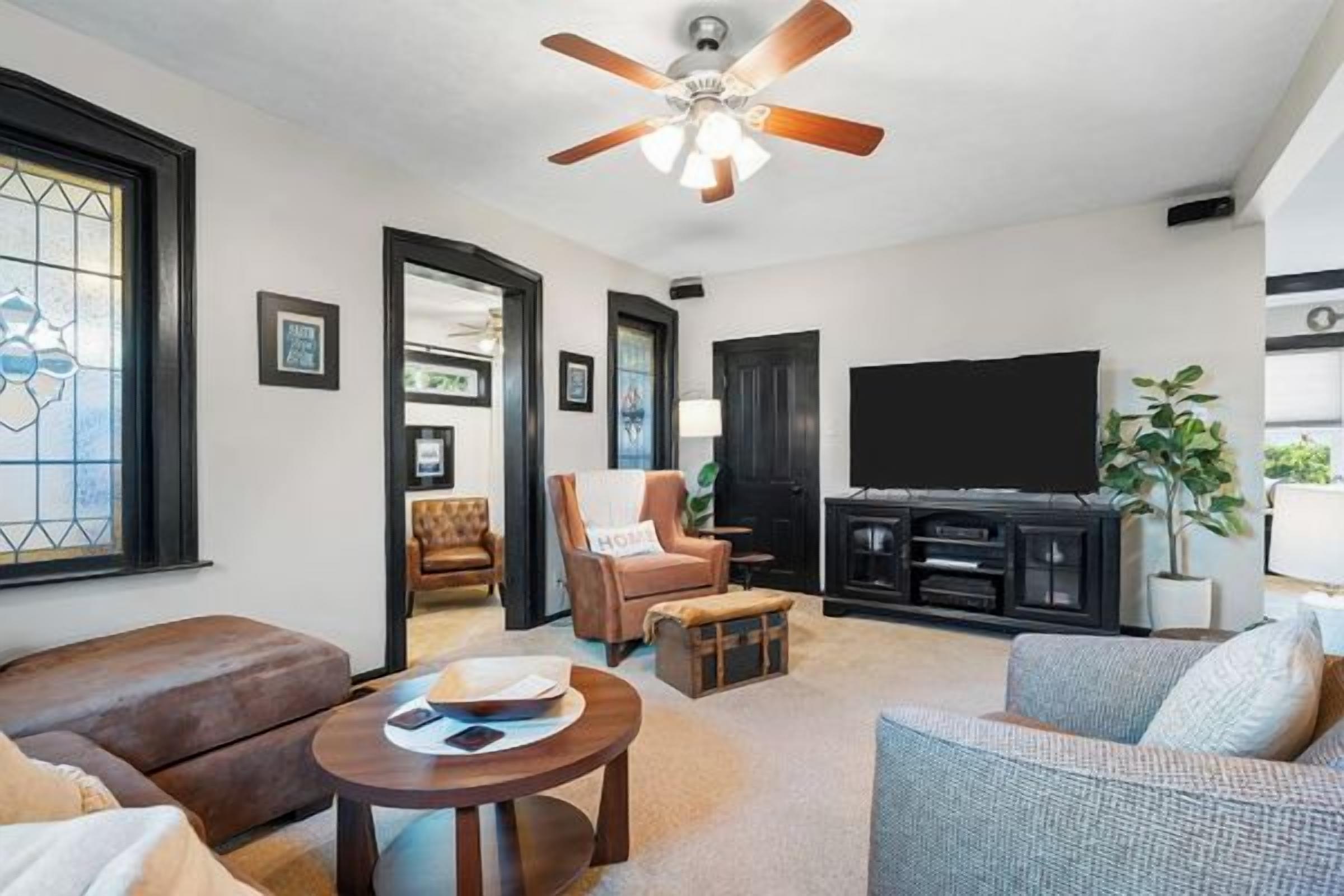A living room with a ceiling fan, a flat-screen TV, and a seating area with a sofa and armchairs.