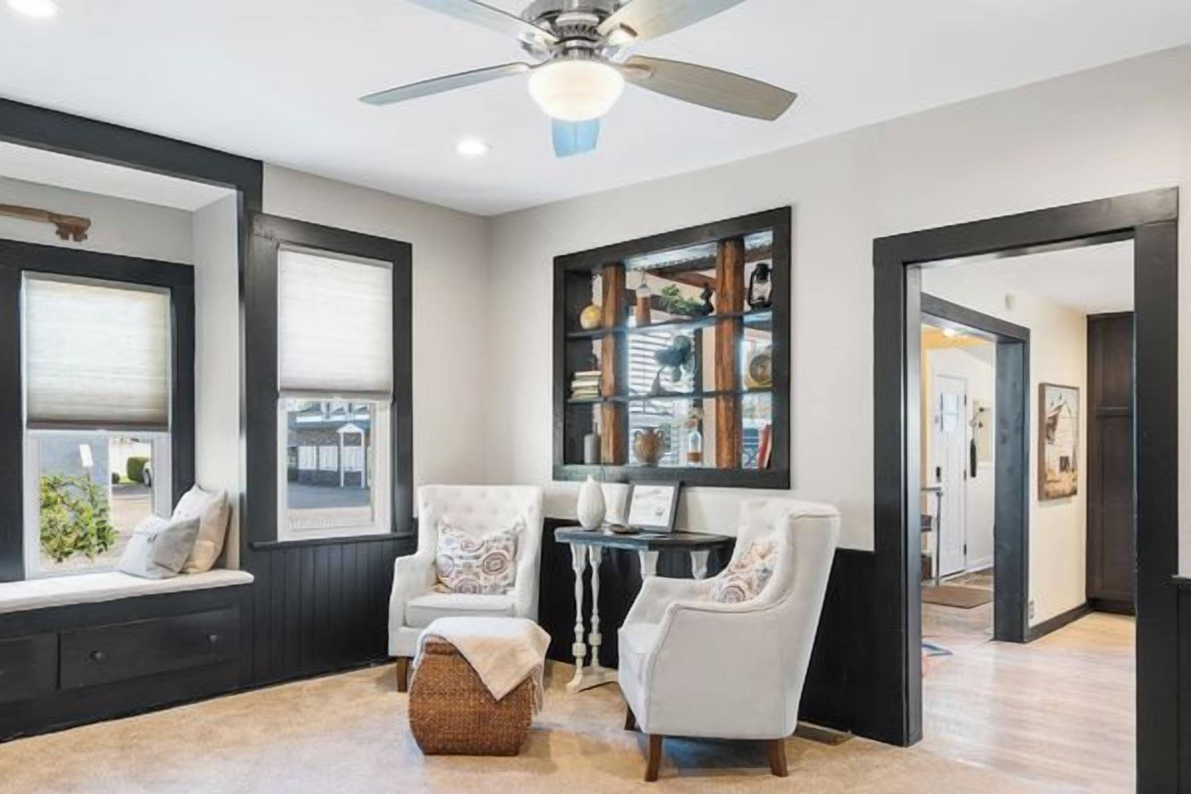 A room with a ceiling fan, a built-in bench with cushions, a side table, and a bookshelf.
