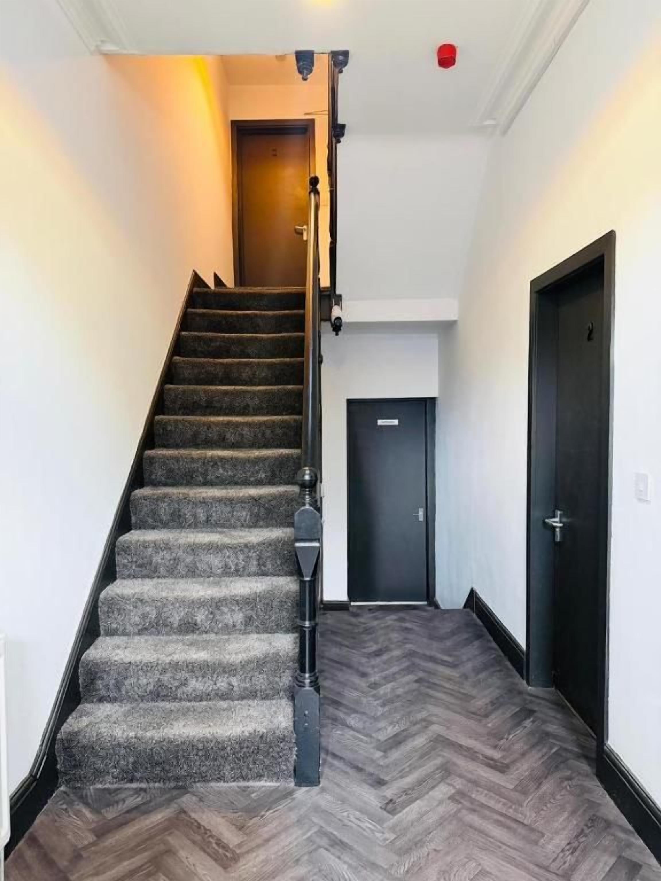 Una escalera alfombrada con barandilla que lleva a una puerta en la parte superior.