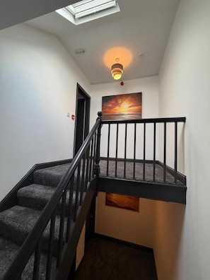 A staircase with a black railing, a ceiling light, and a painting on the wall.