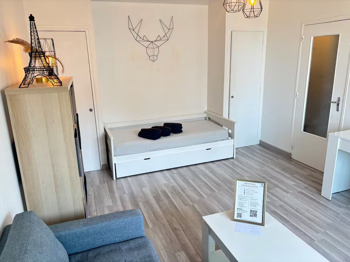Un salon moderne comprenant un canapé, un lit pliant, un élément décoratif mural et une petite table avec un panneau.