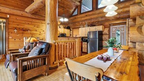 Ein Holzblockhaus-Innenraum mit Esstisch, Stühlen, Küchenzeile und Kamin.