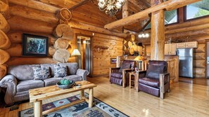 Ein gemütliches Blockhaus-Interieur mit einer Couch, Sesseln, einem Couchtisch und einer Küchenzeile.