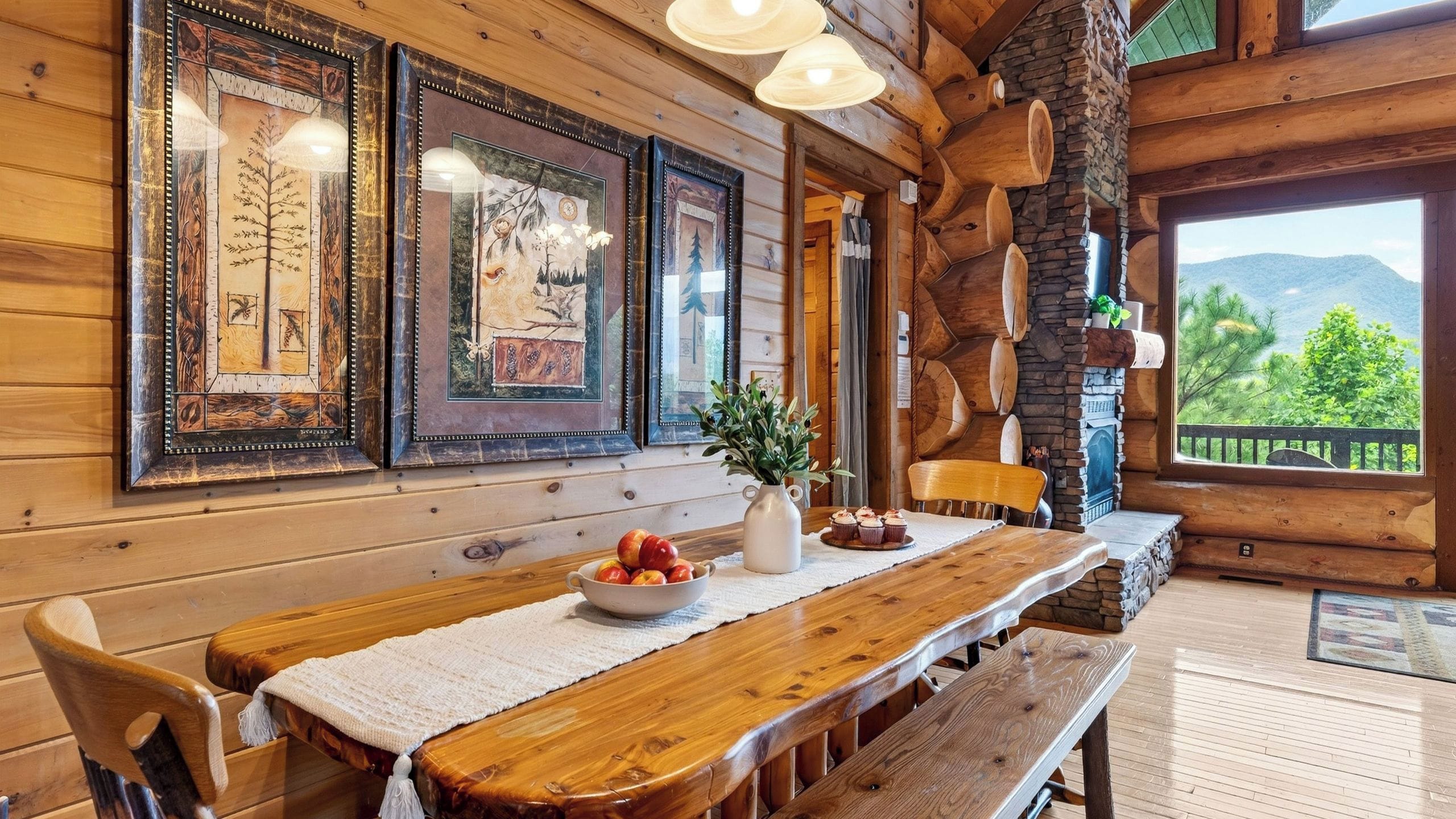 A wooden cabin interior with a dining table, chairs, framed artwork, and a view of the outdoors.