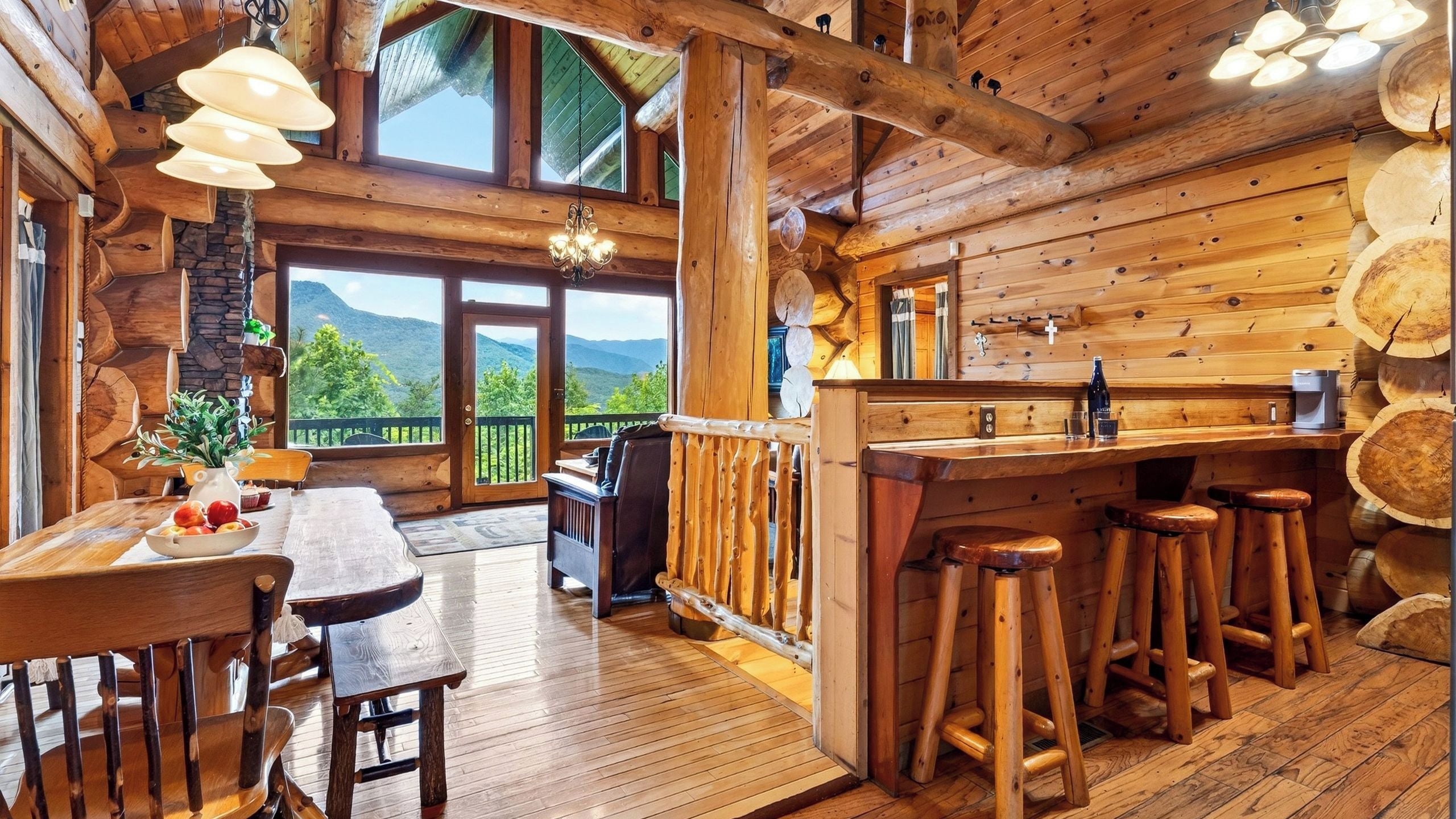 A wooden cabin interior with a dining area, bar stools, and a view of mountains.