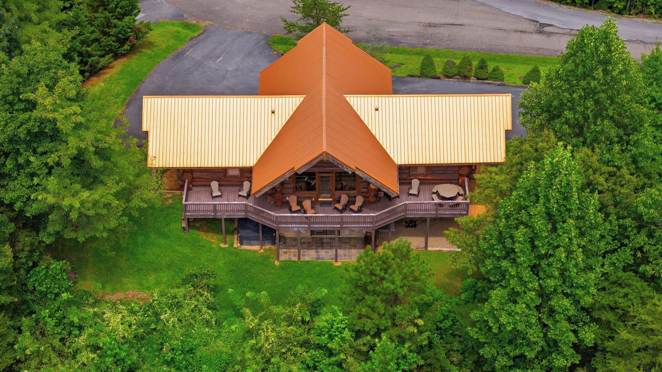 A lodge with a prominent triangular roof, a covered deck with seating, and is surrounded by dense greenery.