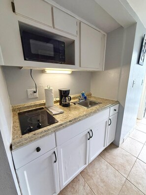A compact kitchen with white cabinets, a built-in microwave, a coffee maker, and a sink. - NEW Amazing Ocean View Studio in Daytona Beach! (Daytona Beach)