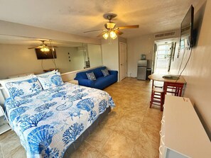 Ein Schlafzimmer mit einem Bett, einem blauen Sofa, einem Schreibtisch, einem Deckenventilator und einem Kühlschrank.