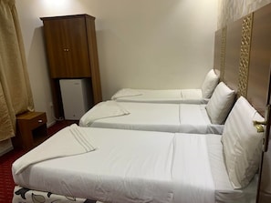 A hotel room with two single beds, a wooden wardrobe, a small refrigerator, and a red carpet. - Maather Elite Hotel (Makkah)