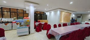 A conference room with tables and chairs, a buffet area with food and drinks, and a large window. - Maather Elite Hotel (Makkah)