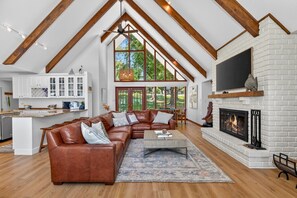 A spacious living room with a large brown leather sectional sofa, a fireplace, and a kitchen with white cabinets and a large window. - The Ranch of Monkey Island [Private Dock] (Afton)