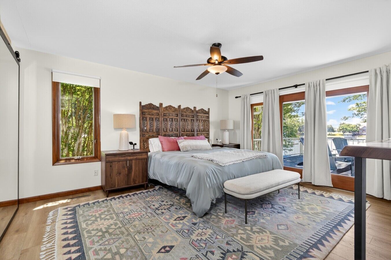 A bedroom with a bed, bedside tables, a ceiling fan, a window, and a view of the outdoors.