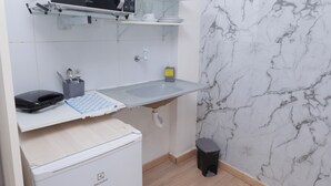 A compact kitchen with a microwave, a small refrigerator, and a marble backsplash. - Pousada Casa da Adriana (Fortaleza)