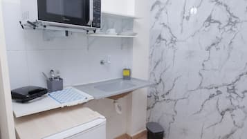 Een compacte keuken met een magnetron, een kleine koelkast en een marmeren achterwand.