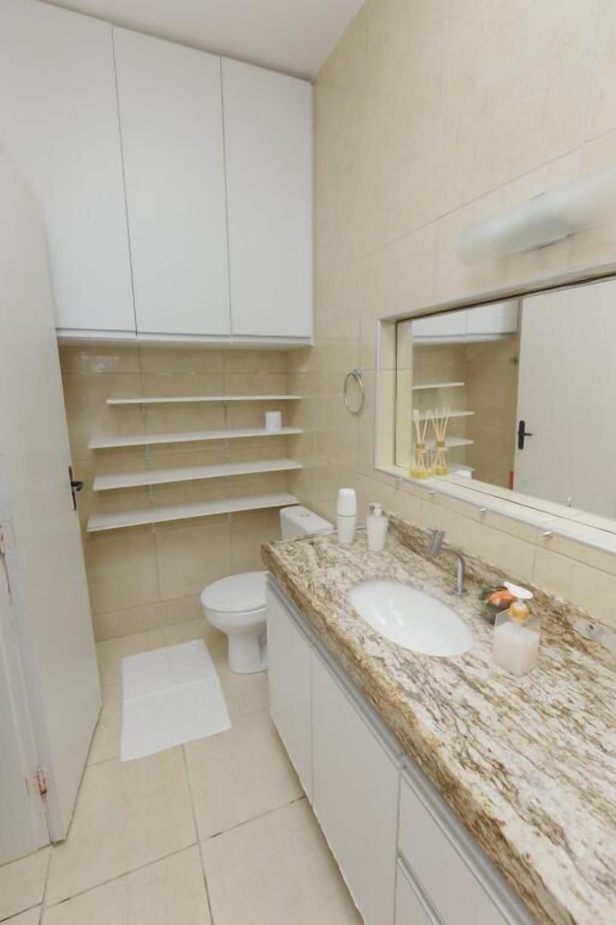 Une salle de bain avec des toilettes blanches, un lavabo doté d’un plan de travail en marbre et un miroir au-dessus du lavabo.