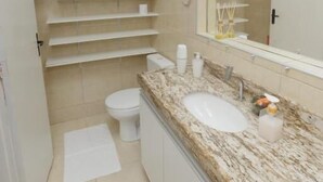 A bathroom with a white toilet, a sink with a marble countertop, and a mirror above the sink. - Pousada Casa da Adriana (Fortaleza)