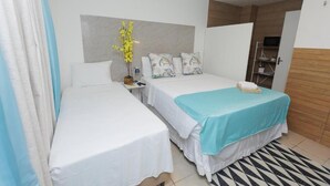 A hotel room with two beds, a wooden headboard, a small table with a vase, and a television in the corner. - Pousada Casa da Adriana (Fortaleza)