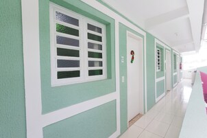 Corredor com paredes verdes, molduras brancas e piso ladrilhado.