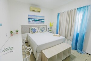 Quarto com cama, escrivaninha, cadeira, mesa de cabeceira, ar-condicionado na parede e janela com cortinas.