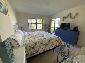 Une chambre à coucher avec un lit, une commode, une télévision et une fenêtre.